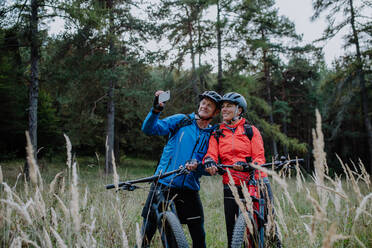 A senior couple bikers using smartphone outdoors in forest in autumn day. - HPIF05445