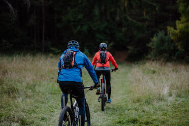 A rear view of active senior couple riding bikes outdoors in forest in autumn day. - HPIF05446