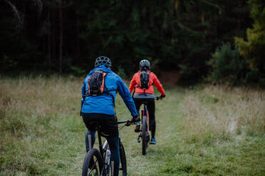 Rückansicht eines aktiven älteren Paares beim Fahrradfahren im Wald an einem Herbsttag. - HPIF05446