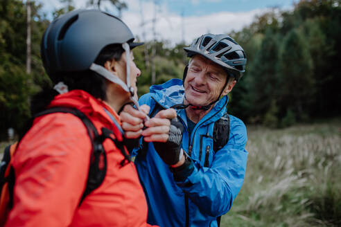 Ein älteres Paar Radfahrer setzen auf Fahrradhelm im Freien im Wald im Herbst Tag. - HPIF05447