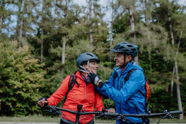 A senior couple bikers putting on cycling helmet outdoors in forest in autumn day. - HPIF05448