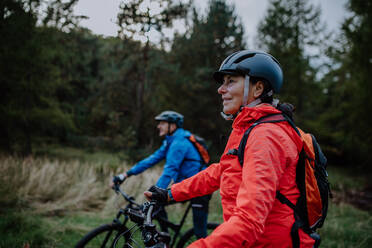 Ein älteres Radlerpaar mit E-Bikes bewundert die Natur im Wald an einem Herbsttag. - HPIF05451