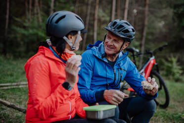 Ein glückliches älteres Paar Radfahrer mit Essen Snack im Freien im Wald im Herbst Tag. - HPIF05457