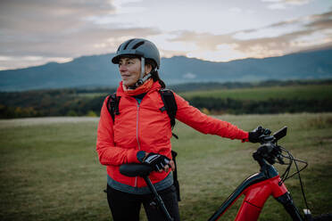 A senior woman biker standing with bike outdoors in nature in autumn day. - HPIF05465