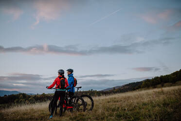 A senior couple bikers with e-bikes admiring nature outdoors in forest in autumn day. - HPIF05467