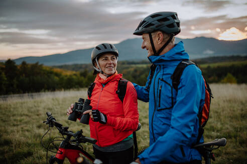 A senior couple bikers with binoculars admiring nature outdoors in meadow in autumn day. - HPIF05470