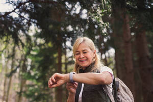 Eine ältere Wanderin, die im Wald in der Natur spazieren geht und eine Smartwatch benutzt. - HPIF05481