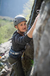 Porträt einer älteren Frau, die auf Felsen klettert und in die Kamera schaut, draußen in der Natur, aktiver Lebensstil. - HPIF05486