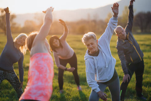 Eine Gruppe von Senioren mit einem Sportlehrer, die bei Sonnenuntergang draußen in der Natur Sport treiben, aktiver Lebensstil. - HPIF05512