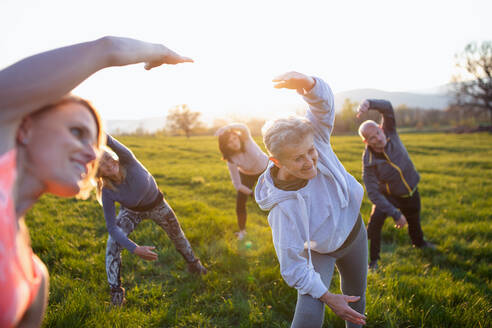 Eine Gruppe von Senioren mit einem Sportlehrer, die bei Sonnenuntergang draußen in der Natur Sport treiben, aktiver Lebensstil. - HPIF05514