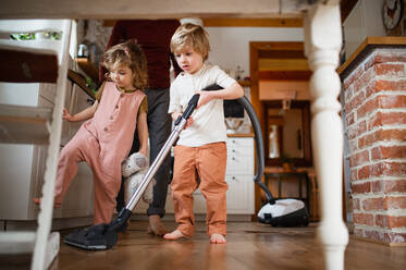 Ein nicht erkennbarer Vater mit zwei kleinen Kindern beim Staubsaugen zu Hause, Konzept der Hausarbeit. - HPIF05516