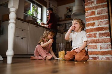 Zwei glückliche kleine Kinder mit ihrem Vater zu Hause, die auf dem Boden Cornflakes essen. - HPIF05519