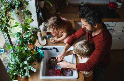 Draufsicht auf einen Vater mit zwei kleinen Kindern, der zu Hause Geschirr spült, Konzept für die tägliche Arbeit. - HPIF05520