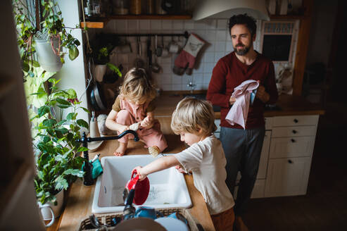 Ein reifer Vater mit zwei kleinen Kindern wäscht zu Hause das Geschirr, Konzept für die tägliche Arbeit. - HPIF05521