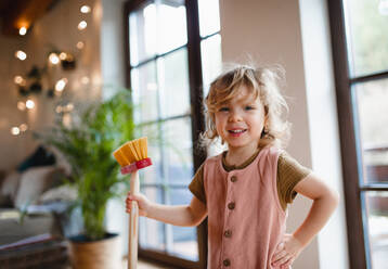 A small girl with broom helping with housework indoors at home, looking at camera. - HPIF05522