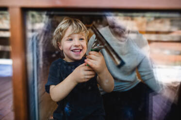 Ein glücklicher Junge mit unerkennbarem Vater putzt Fenster zu Hause, Hausarbeit Konzept. - HPIF05525