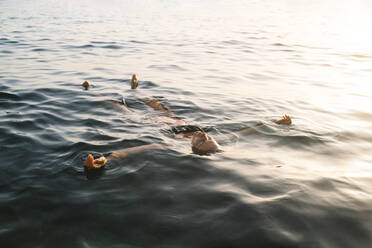 Frau schwimmt bei Sonnenuntergang auf dem Meer - MMPF00577