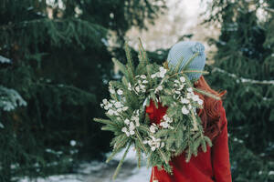 Woman wearing knit hat holding wreath in front of trees - VSNF00211