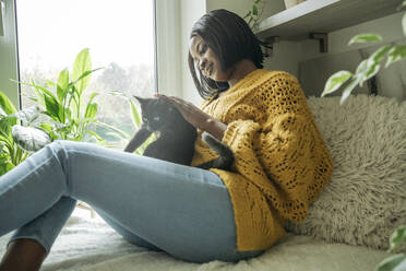 Smiling woman with cat sitting by window at home - OSF01241