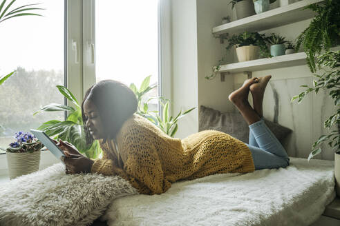 Young woman using tablet PC lying by window at home - OSF01244