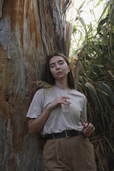 Junge Frau mit geschlossenen Augen lehnt sich an einen alten Baumstamm - SYEF00182