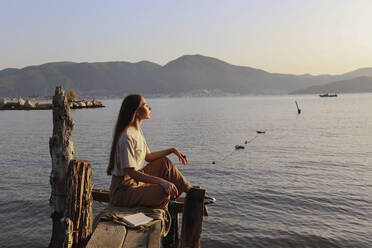 Frau sitzt auf handgefertigter Fischerplattform vor dem Meer - SYEF00184
