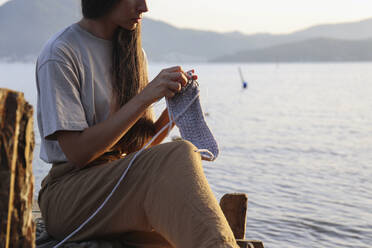 Junge Frau strickt vor dem Meer - SYEF00185