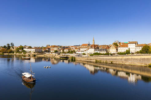 France, Nouvelle-Aquitaine, Bergerac, Boat sailing along Dordogne River with old town buildings in background - WDF07208