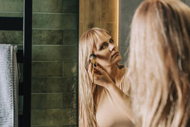 Blond woman applying make-up with brush in bathroom - VSNF00216