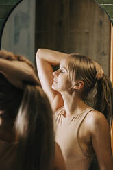 Blonde Frau mit geschlossenen Augen hält Haare im Badezimmer - VSNF00220