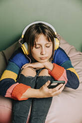 Girl wearing headphones using smart phone at home - VSNF00231