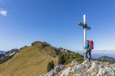 Germany, Bavaria, Female hiker touching summit cross on Kaserwand mountain - FOF13365