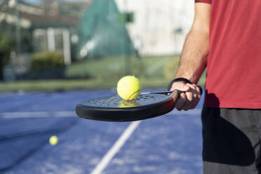 Männerhand hält Tennisschläger und Ball auf einem Sportplatz - FMOF01611