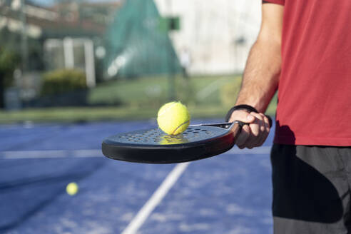 Männerhand hält Tennisschläger und Ball auf einem Sportplatz - FMOF01611
