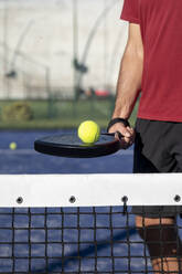 Männerhand hält Tennisschläger und Ball auf einem Sportplatz an einem sonnigen Tag - FMOF01612