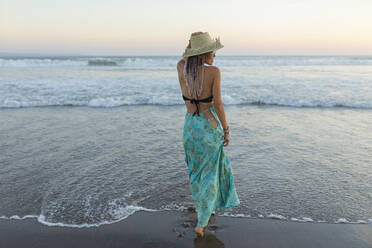 Junge Frau mit Hut steht vor dem Meer am Strand - EAF00137