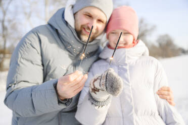 Glücklicher Vater und Tochter halten Wunderkerzen im Winter - EYAF02409
