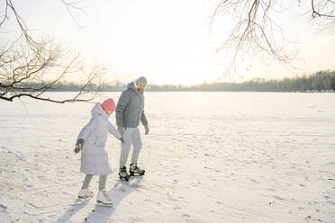 Father and daughter doing ice skating on frozen lake in winter - EYAF02411