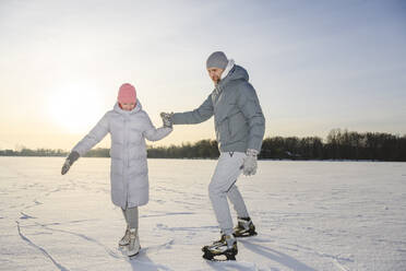 Happy girl with father practicing ice skating on winter lake - EYAF02412