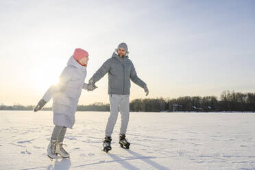 Happy daughter with father practicing ice skating on winter lake - EYAF02413