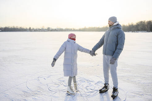 Vater hält die Hände seiner Tochter und übt Schlittschuhlaufen auf einem winterlichen See - EYAF02416