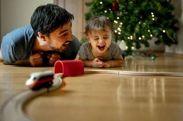 Fröhlicher Vater und Sohn spielen zu Hause mit einer Spielzeugeisenbahn - ANAF00759