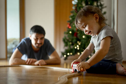 Glücklicher Sohn und Vater spielen zu Hause mit einer Spielzeugeisenbahn - ANAF00761