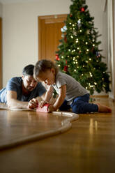 Vater und Sohn spielen mit einem hölzernen Spielzeugzug vor dem Weihnachtsbaum zu Hause - ANAF00763