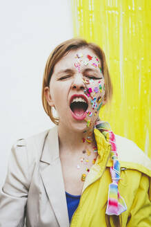 Woman with stickers on face screaming in front of wall - SVCF00263