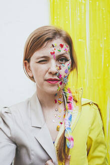 Frau mit Aufklebern im Gesicht zwinkert vor einer zweifarbigen Wand - SVCF00269