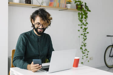 Smiling businessman using mobile phone at desk - XLGF03127