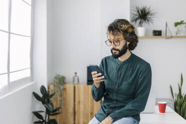 Freelancer using smart phone sitting on desk in office - XLGF03131