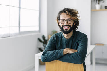 Happy freelancer sitting on chair in office - XLGF03137