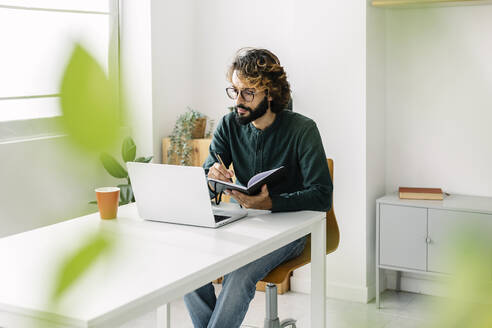 Freelancer with pen and diary using laptop at desk - XLGF03148